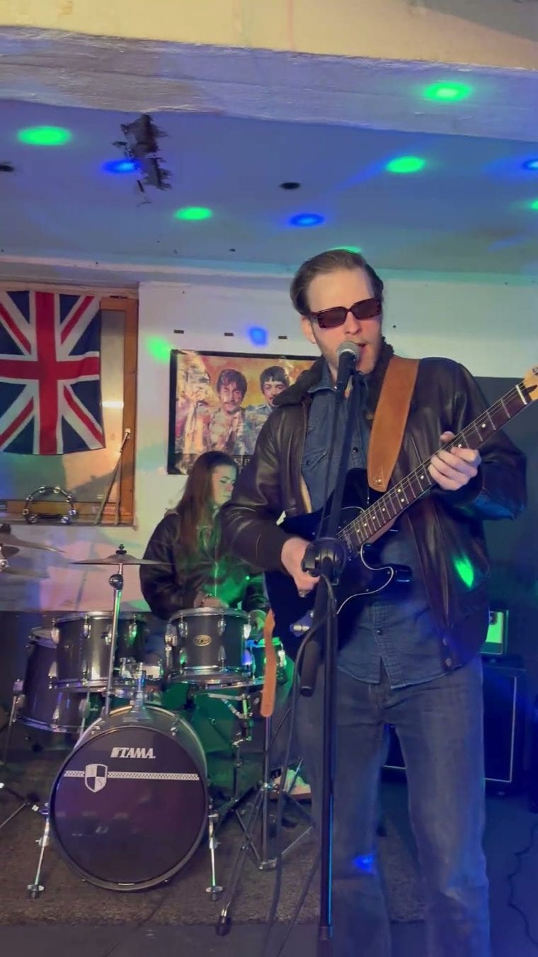 Sänger mit Gitarre, Schlagzeugerin und Union-Jack-Flagge im Hintergrund